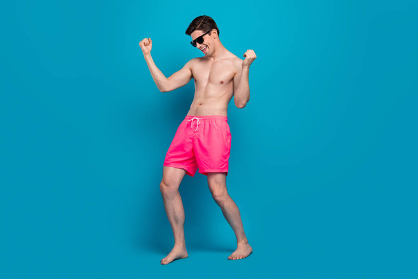Photo of crazy carefree guy dance clubbing celebrate victory wear sunglass swimwear shorts isolated blue color background - Zdjęcie, obraz