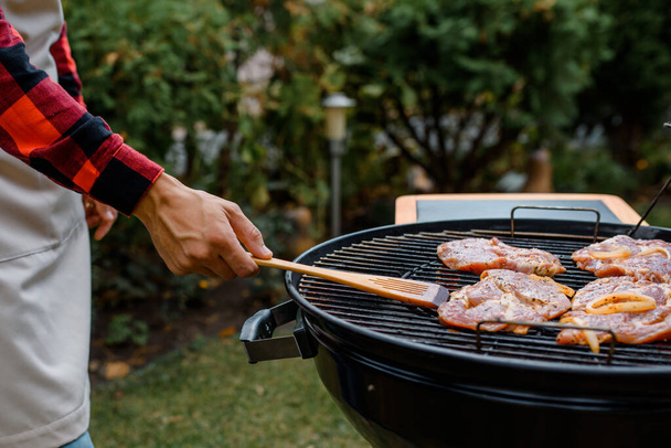 Fermez la main tenant une spatule en bois et cuisinez un barbecue sur un gril. - Photo, image