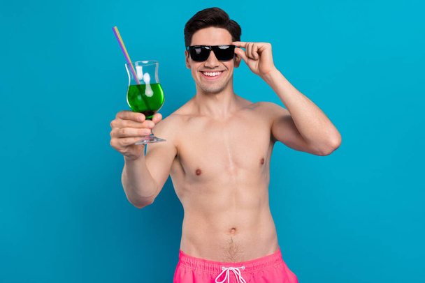 Photo of cheerful guy hold cocktail enjoy bar drink wear sunglass swimwear shorts isolated blue color background - Foto, Imagen