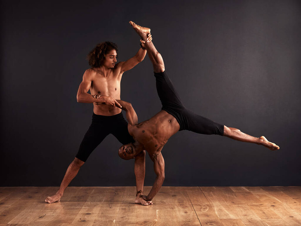Trust and strength. Two male contemporary dancers performing a dramatic pose in front of a dark background. - Фото, изображение