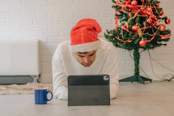 άνδρας στο σπίτι τα Χριστούγεννα με το καπέλο και τον υπολογιστή του Άγιου Βασίλη - Φωτογραφία, εικόνα