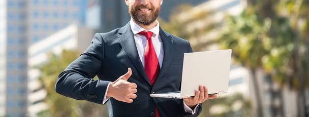 обрізаний бізнесмен у формальному одязі тримає комп'ютер за межами офісу, показуючи великий палець вгору, мережа
. - Фото, зображення