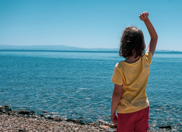 petite fille debout seule près de la plage et jetant des pierres à la mer - Photo, image