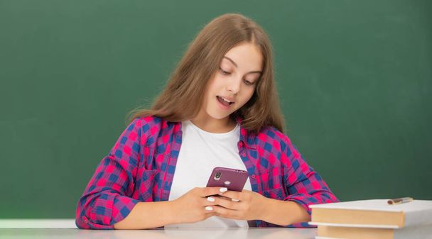 χαρούμενο παιδί κουβεντιάζοντας στο smartphone στην τάξη στον πίνακα, μήνυμα - Φωτογραφία, εικόνα