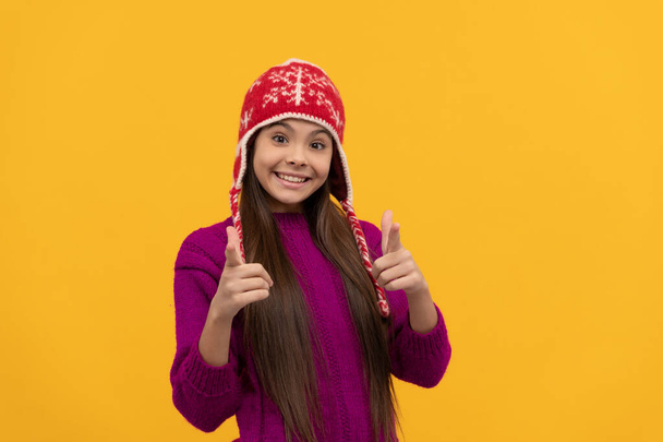 smiling teen girl wear knitted hat pointing finger, keep warm - Photo, Image