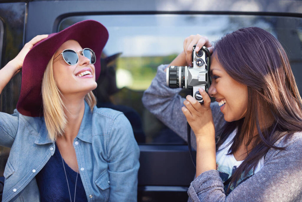 Pictures of play. Shot of a two girlfriends taking photos of themselves while on a roadtrip. - Photo, Image
