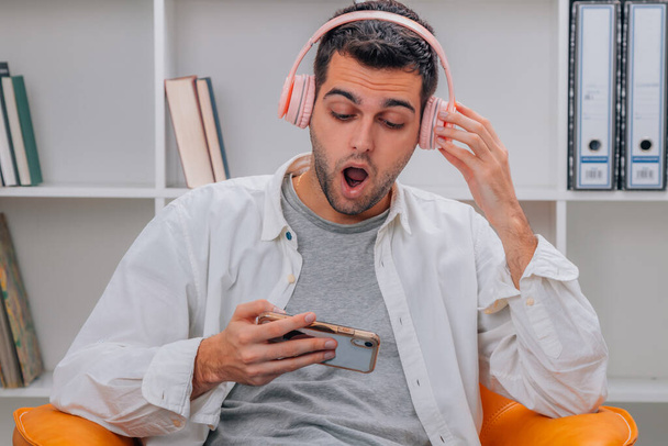 csodálkozó férfi otthon hallgat zenét fejhallgatóval és mobiltelefonnal - Fotó, kép