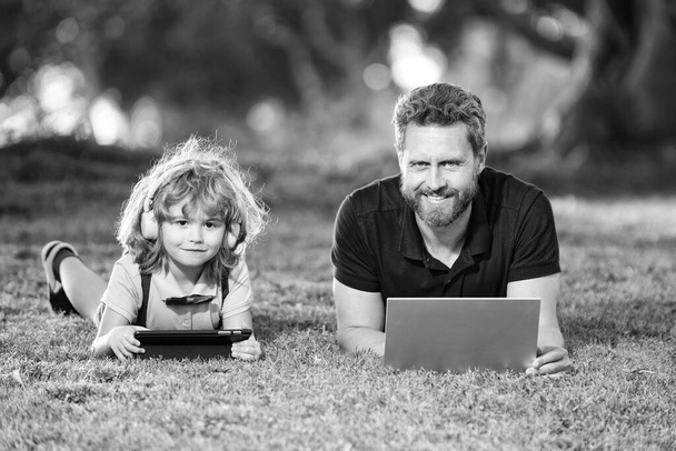 apa és fia használja laptop videohívás vagy lecke zenét hallgatni fejhallgató a parkban, család. - Fotó, kép