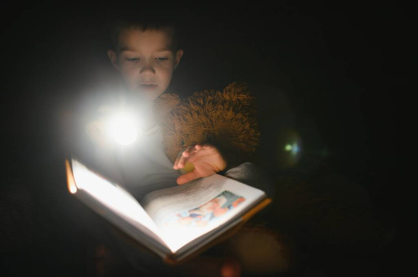 Child reading book in bed. Kids read at night. Little boy with fairy tale books in bedroom . Education for young children. Bedtime story in the evening. Cute kid under blanket in dark room with lamp. - Fotografie, Obrázek