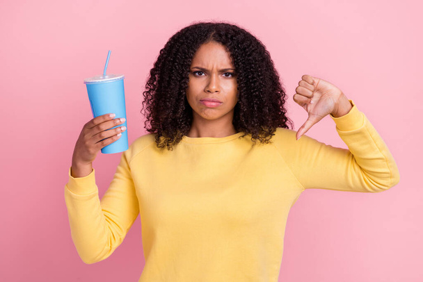 Photo of upset bad dark skin woman wear yellow sweater holding cup showing thumb down face isolated pink color background - Fotó, kép