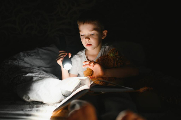 Child reading book in bed. Kids read at night. Little boy with fairy tale books in bedroom . Education for young children. Bedtime story in the evening. Cute kid under blanket in dark room with lamp. - Foto, Bild