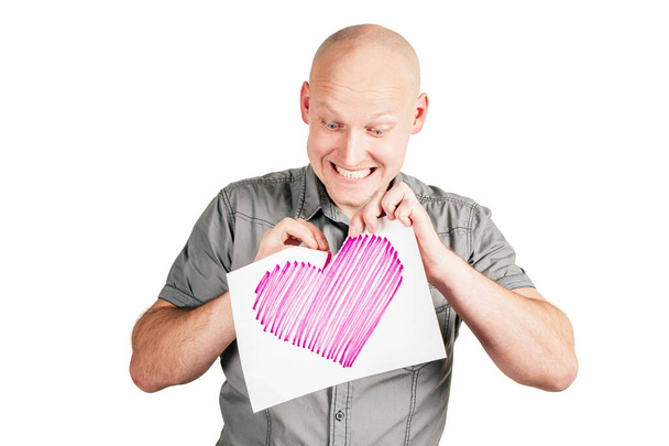 Homme chauve souriant en chemise grise déchirure coeur rose dessiné sur feuille de papier avec plaisir isolé sur fond blanc. - Photo, image