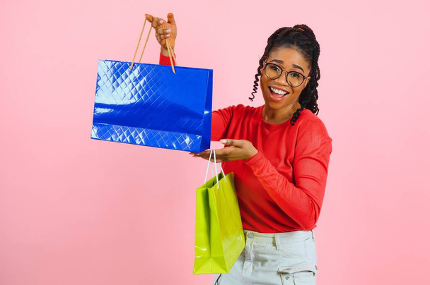 Jonge zwarte vrouw met boodschappentassen op roze backgrond - Foto, afbeelding