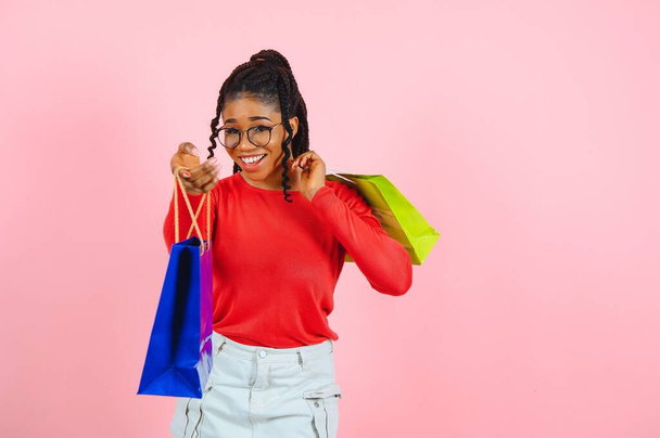 Sale Concept. Excited afro girl holding cheek and shopping bags looking aside with open mouth, pink wall, copyspace - 写真・画像