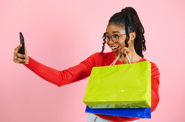 Young black woman holding shopping bags on pink backgrond - Fotó, kép
