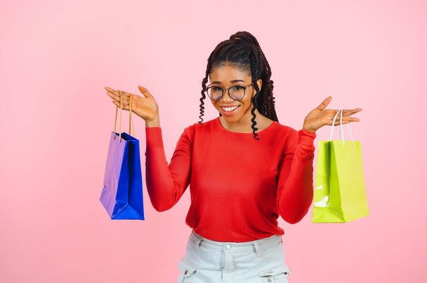 Giovane donna nera che tiene borse della spesa sul retro rosa - Foto, immagini