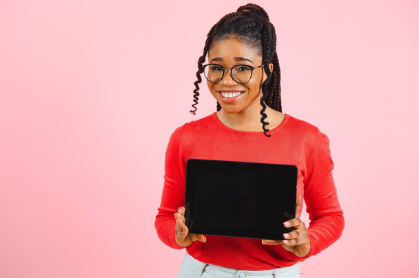 Young american student girl with curly african hair holding digital tablet and smiling standing over isolated pink background with copy space for text, logo or advertising. - Photo, image