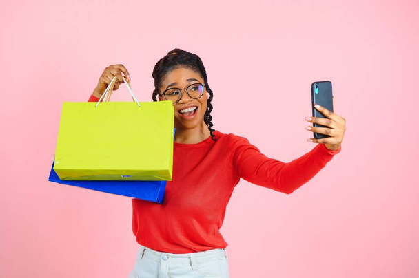 Jovem mulher negra segurando sacos de compras no fundo rosa - Foto, Imagem