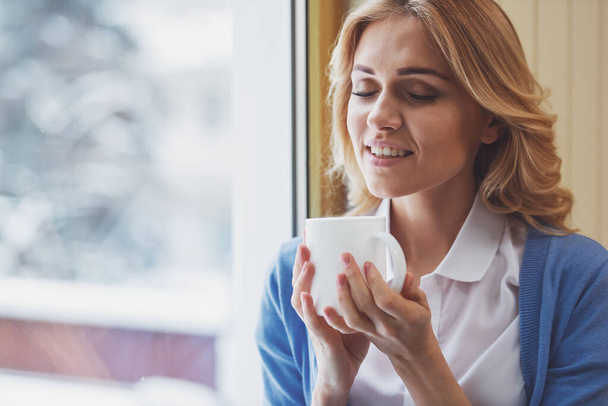 Retrato de uma bela jovem segurando uma xícara e apreciando o aroma do café
 - Foto, Imagem