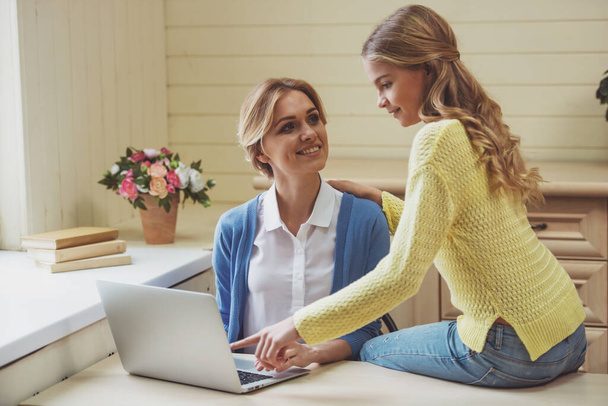 Hermosa adolescente que muestra a su hermosa madre cómo utilizar un ordenador portátil. Ambos sonriendo mientras están sentados en casa
. - Foto, imagen