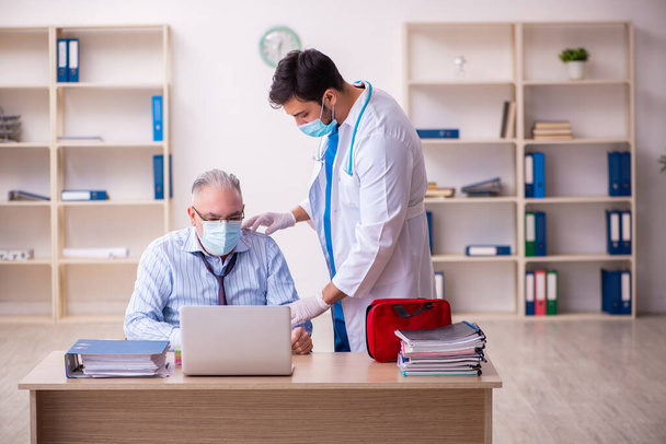 Young male doctor visiting old businessman at workplace - Photo, Image