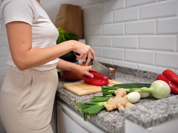 взрослая женщина разрабатывает овощное блюдо, расщепляет красный перец на деревянной доске - Фото, изображение