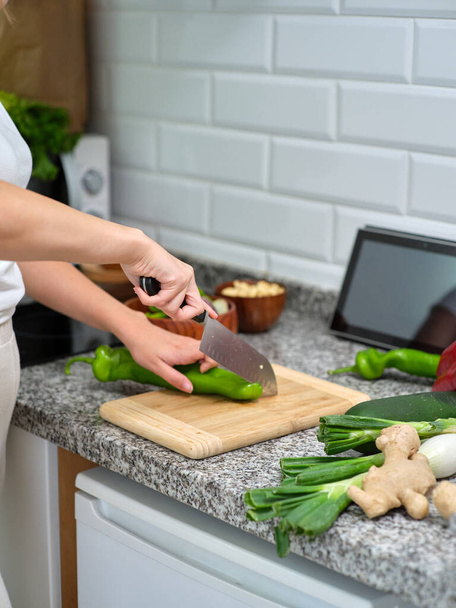 cozinhar cortar legumes em uma tábua de madeira, tablet encostado à parede para ver a receita - Foto, Imagem