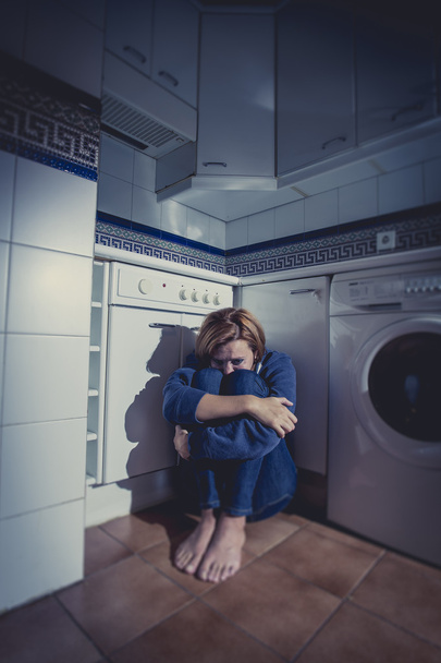 eenzame en zieke vrouw zittend op de keukenvloer in depressie stress en verdriet - Foto, afbeelding