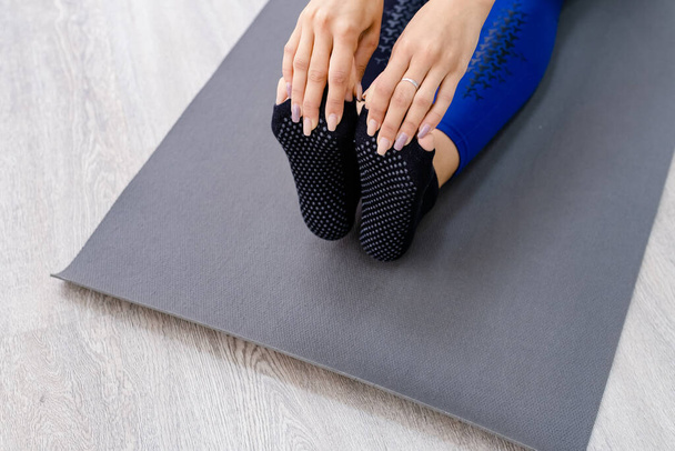 Gros plan Vue du dessus des mains tenant le pied d'une femme assise sur un tapis de yoga à l'extérieur sur un plancher de bois - Photo, image