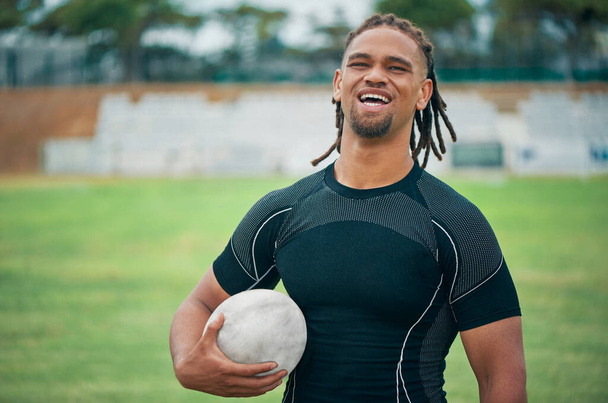 Rugby is my thing. Cropped portrait of a handsome young rugby player smiling while holding a rugby ball on the field. - 写真・画像