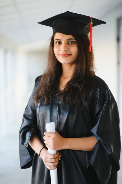 Happy Indian university student in graduation gown and cap holding diploma certificate. - Foto, Bild