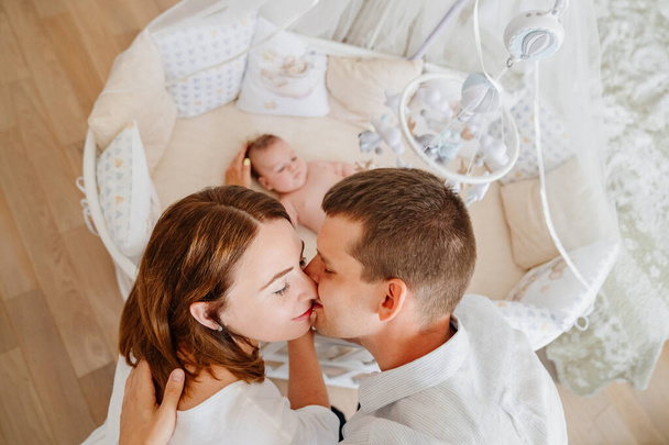 view from above. parents at a baby lies in a white crib with mobile with toys. - Foto, Imagen
