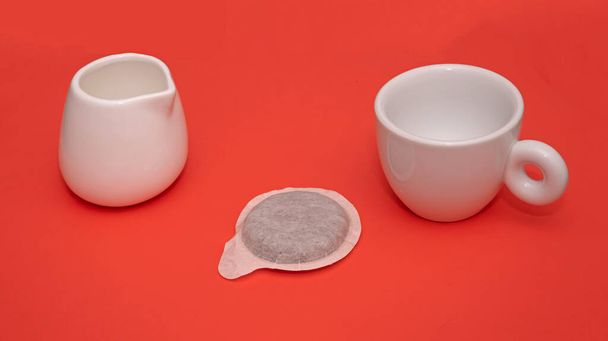 Small ceramic espresso cup with pod and milk doser on red background - Valokuva, kuva