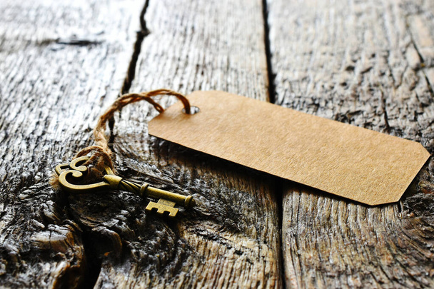 Ein flaches Bild eines kleinen Messingschlüssels mit braunem Papieretikett auf einer alten hölzernen Tischplatte.  - Foto, Bild