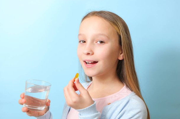 Una adolescente sostiene una cápsula de omega 3 en sus manos sobre un fondo de color.  - Foto, Imagen