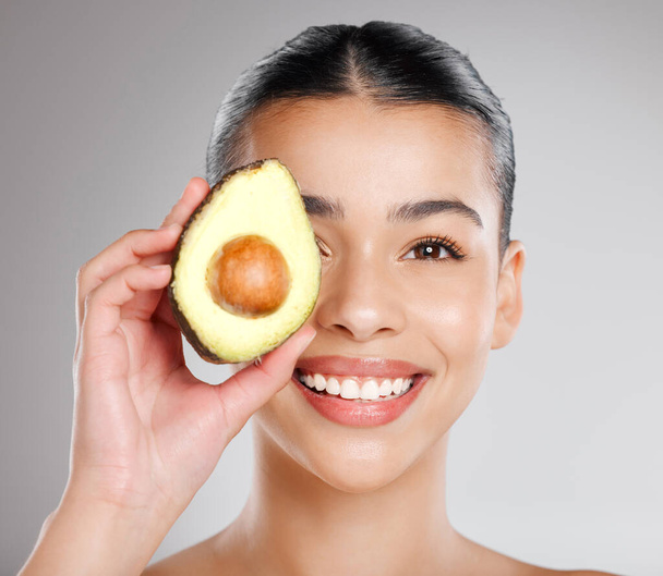 Hallo Hautpflege Kraftpaket avo. Studioaufnahme einer attraktiven jungen Frau, die sich vor grauem Hintergrund eine Avocado ins Gesicht hält. - Foto, Bild