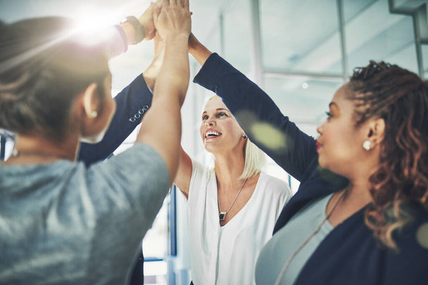 Success is shining on this team. Shot of a diverse group of coworkers high fiving together in an office. - Photo, Image