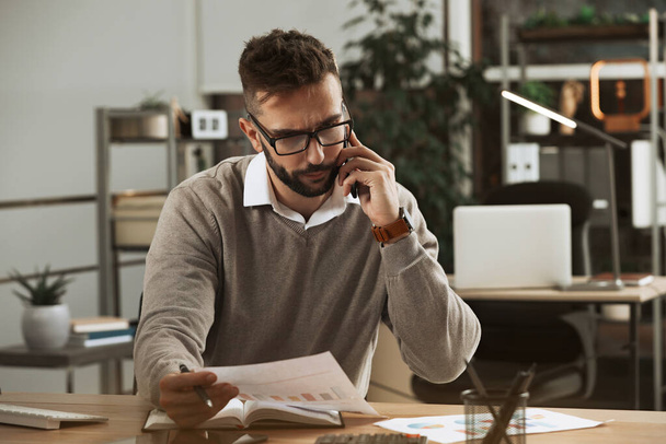 Man talking on phone while working with documents at table in office - Foto, Imagem