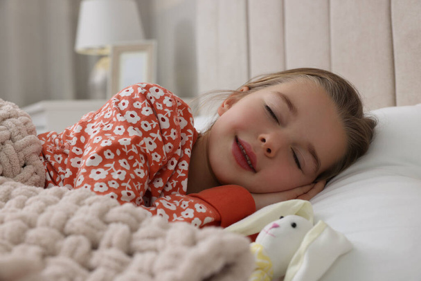 Cute little girl with toy bunny sleeping in bed at home - 写真・画像