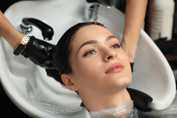 Hairdresser rinsing out dye from woman's hair in beauty salon - Photo, image