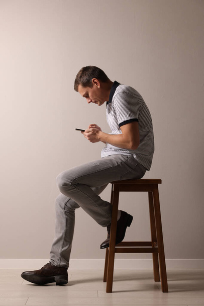 Man with bad posture using smartphone while sitting on stool against grey background - Foto, Imagen
