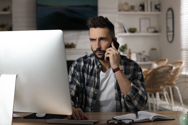 Man talking on phone while working with computer at table in home office - Foto, immagini