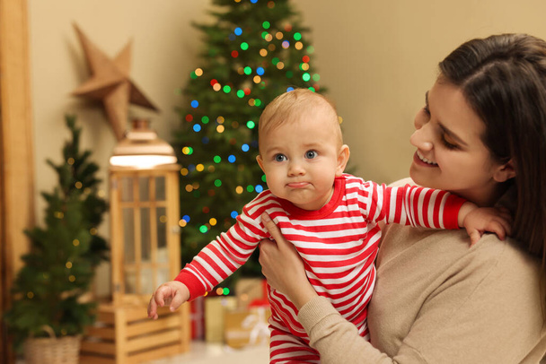 Happy young mother with her cute baby in room decorated for Christmas. Winter holiday - Φωτογραφία, εικόνα