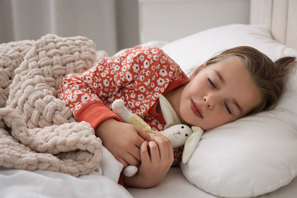 Cute little girl with toy bunny sleeping in bed at home - Фото, изображение