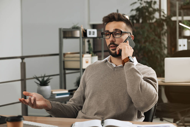 Man talking on phone while working at table in office - Photo, Image