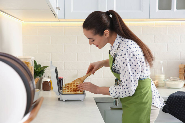 Woman making delicious Belgian waffles in kitchen - Zdjęcie, obraz