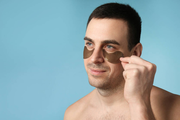 Young man applying under eye patches on light blue background. Space for text - Fotó, kép