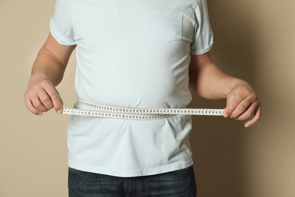 Man measuring waist with tape on beige background, closeup - Fotó, kép