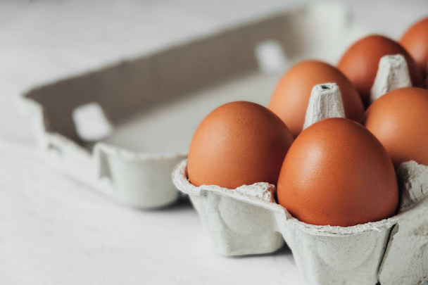 Kahverengi tavuk yumurtaları beyaz ahşap masada karton tepside. Yumurtalı açık bir konteynırın yan görünümü. - Fotoğraf, Görsel