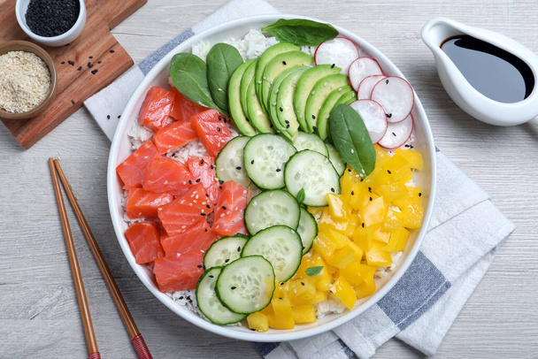 Delicious poke bowl with salmon and vegetables served on wooden table, flat lay - 写真・画像